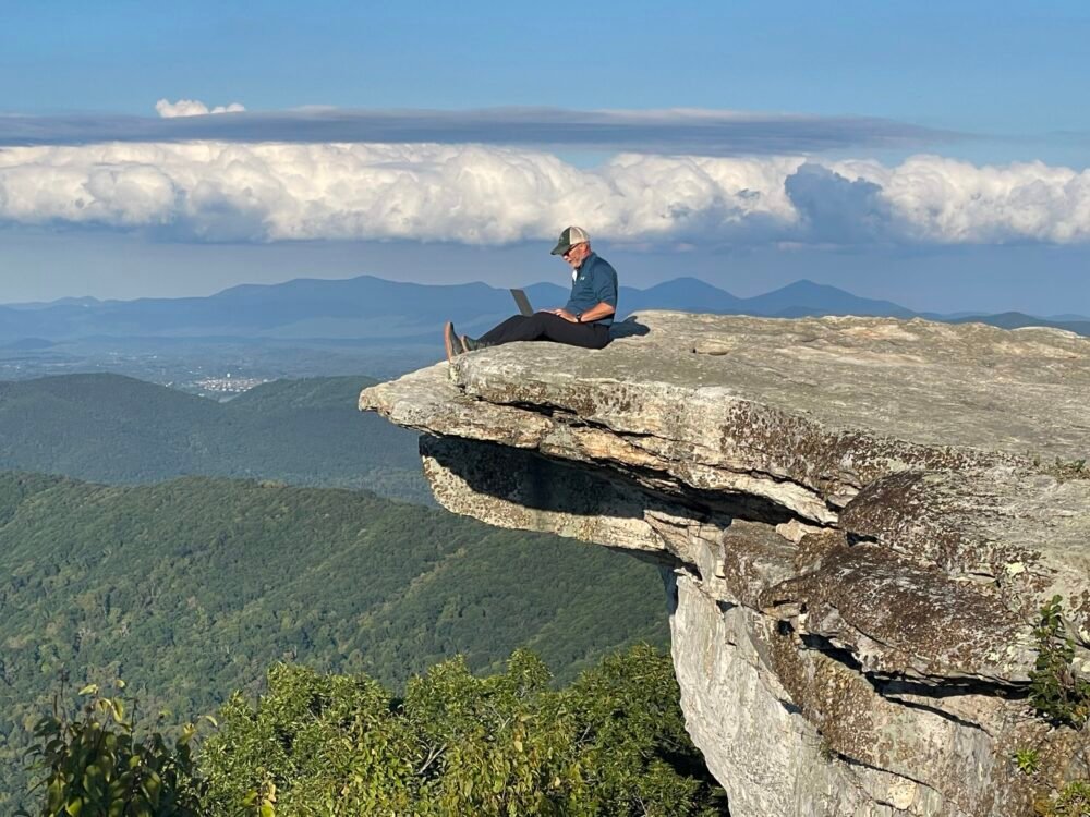 Hiker sitting with laptop on McAfee Knob